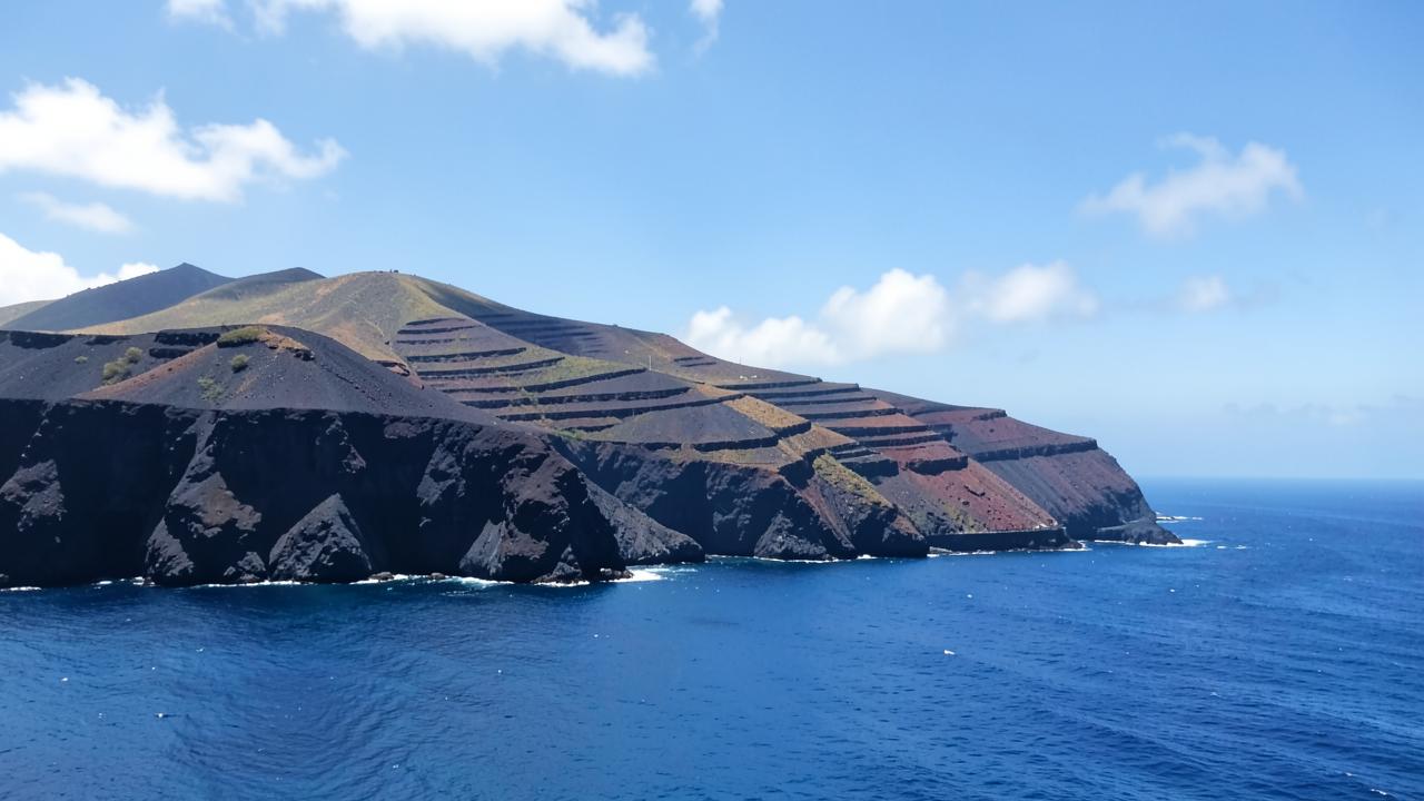 Costa vulcânica de ilha atlântica com falésias escuras e mar azul profundo
